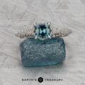 The "Anya" ring in 14k white gold, featuring a 0.74-carat Montana sapphire, rests on a rough blue crystal atop a textured gray surface with the Earth’s Treasury logo below.
