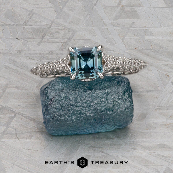 The "Anya" ring in 14k white gold with 0.74-carat Montana sapphire The "Anya" ring in 14k white gold, featuring a 0.74-carat Montana sapphire, rests on a rough blue crystal atop a textured gray surface with the Earth’s Treasury logo below.