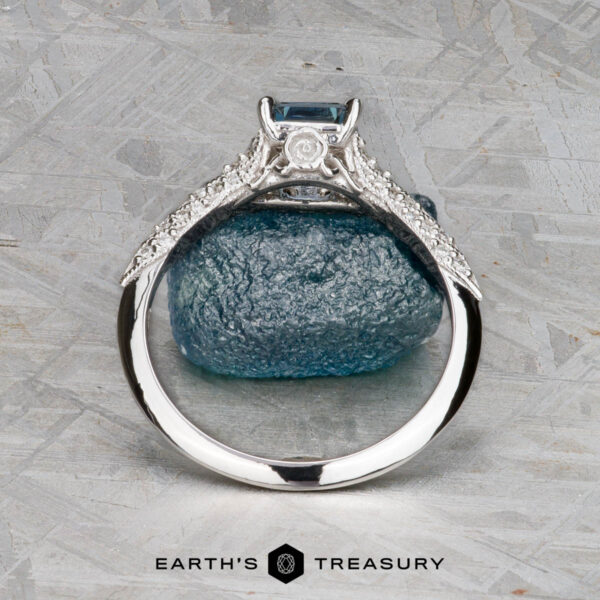 The "Anya" ring in 14k white gold with 0.74-carat Montana sapphire The "Anya" ring in 14k white gold features a 0.74-carat Montana sapphire in a square setting with side diamonds, displayed upright before a blue stone. Below, the words "Earth's Treasury" appear.