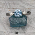 The Braided "Zuri" ring in 14k white gold, featuring a 1.15-carat Montana sapphire, is displayed on a rough blue crystal atop a textured gray surface.