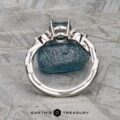 The Braided "Zuri" ring in 14k white gold with a 1.15-carat Montana sapphire is displayed upright on a rough blue stone, set on a textured gray surface with the Earth’s Treasury logo beneath.