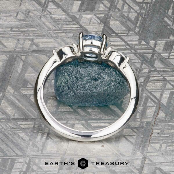 The "Zuri" ring in platinum with 0.87-carat Montana sapphire The "Zuri" ring in platinum with a 0.87-carat Montana sapphire is displayed upright on a textured gray surface, with the "Earth's Treasury" logo and text at the bottom.