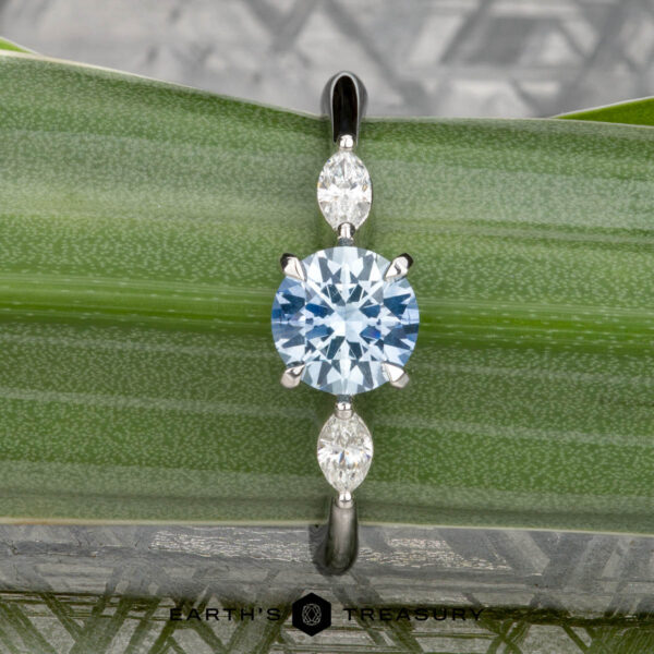 The "Zuri" ring in platinum with 0.87-carat Montana sapphire The "Zuri" ring in platinum features a 0.87-carat Montana sapphire center and two marquise-cut clear stones, beautifully displayed on a green leaf background.