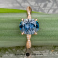 The "Musette" ring in 20k pink gold features a 3.21-carat Montana sapphire atop a twisted diamond band, showcased on a green leaf with "EARTH'S TREASURY" displayed at the bottom.