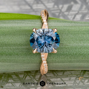 The "Musette" ring in 20k pink gold features a 3.21-carat Montana sapphire atop a twisted diamond band, showcased on a green leaf with "EARTH'S TREASURY" displayed at the bottom.
