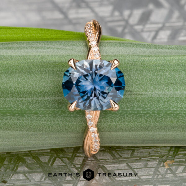 The "Musette" ring in 20k pink gold with 3.21-carat Montana sapphire The "Musette" ring in 20k pink gold features a 3.21-carat Montana sapphire atop a twisted diamond band, showcased on a green leaf with "EARTH'S TREASURY" displayed at the bottom.