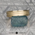 The "Silas" band in 14k yellow gold rests atop a rough blue gemstone on a patterned gray background, with the text "EARTH'S TREASURY" below.
