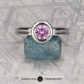 The "Lola" ring in 14k white gold, featuring a 0.71-carat round Montana sapphire, is displayed upright on a rough blue stone with a geometric background and the Earth's Treasury logo at the bottom.