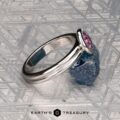 The "Lola" ring in 14k white gold with a 0.71-carat Montana sapphire rests on a rough blue stone atop a patterned metallic surface. "EARTH'S TREASURY" appears at the bottom.