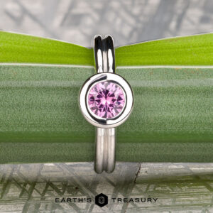 The "Lola" ring in 14k white gold, featuring a 0.71-carat Montana sapphire, is displayed vertically against a green plant stem with the "Earth's Treasury" logo at the bottom.