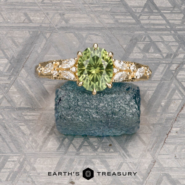 The "Chrysanthemum" ring in 14k yellow gold with 1.46-carat Australian sapphire The "Chrysanthemum" ring, crafted in 14k yellow gold with a 1.46-carat Australian sapphire, is displayed atop a rough blue crystal against a textured gray background.
