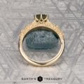 The "Chrysanthemum" ring in 14k yellow gold, featuring a 1.46-carat Australian sapphire, is displayed upright before a textured blue stone on a patterned metallic surface. Logo reads "Earth's Treasury.