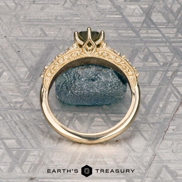 The "Chrysanthemum" ring in 14k yellow gold with 1.46-carat Australian sapphire The "Chrysanthemum" ring in 14k yellow gold, featuring a 1.46-carat Australian sapphire, is displayed upright before a textured blue stone on a patterned metallic surface. Logo reads "Earth's Treasury.