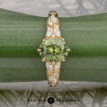 The "Chrysanthemum" ring in 14k yellow gold, featuring a 1.46-carat Australian sapphire and marquise-cut white accent stones, is displayed on a green plant leaf with the "Earth's Treasury" logo below.