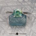The Cathedral "Fleur" platinum ring with a 1.72-carat Montana sapphire is displayed on a rough blue stone, set against a textured metallic background with geometric patterns. The Earth's Treasury logo appears at the bottom.