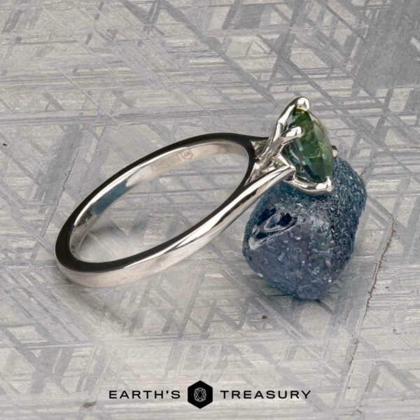 The Cathedral "Fleur" ring in platinum with 1.72-carat Montana sapphire The Cathedral "Fleur" ring in platinum, featuring a 1.72-carat Montana sapphire, rests on a rough blue stone against a patterned metallic background.