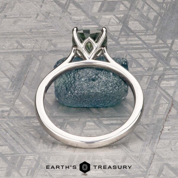 The Cathedral "Fleur" ring in platinum with 1.72-carat Montana sapphire The Cathedral "Fleur" ring in platinum features a 1.72-carat Montana sapphire in an intricate prong setting, displayed upright on a textured blue-gray stone background. Logo text at the bottom reads "Earth's Treasury.