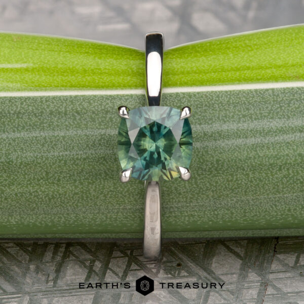 The Cathedral "Fleur" ring in platinum with 1.72-carat Montana sapphire The Cathedral "Fleur" ring in platinum with a 1.72-carat Montana sapphire is displayed upright against two stacked green leaves, with the "Earth's Treasury" logo and text at the bottom.