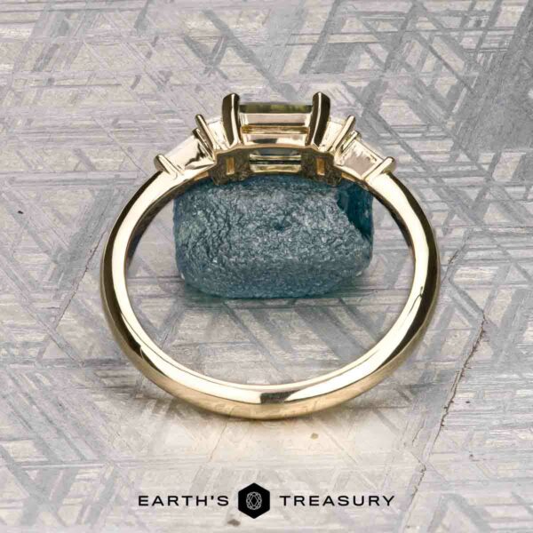 The "Athena" ring in 14K yellow gold with 1.20-carat Montana sapphire The "Athena" ring in 14K yellow gold with a 1.20-carat Montana sapphire stands upright against a blue mineral and geometric background, with the "EARTH'S TREASURY" logo at the bottom.
