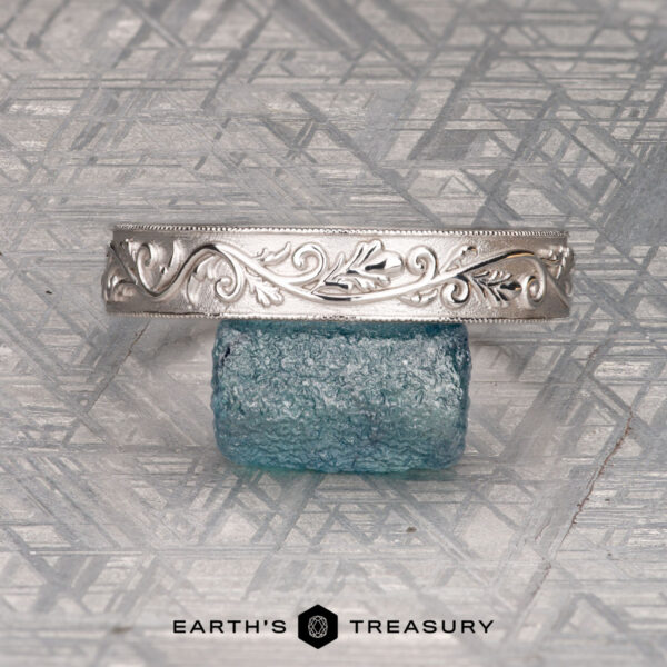 The "Oakley" ring in 14K white gold The "Oakley" ring in 14K white gold displayed on a textured blue glass block, set against a geometric patterned background. Earth's Treasury logo at the bottom.