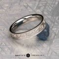 The "Oakley" ring in 14K white gold, engraved with a floral pattern, rests atop a rough blue gemstone on a textured surface, with "Earth's Treasury" displayed below.