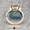 The "Dinara" ring in 14K yellow gold, featuring a 1.72-carat Australian sapphire, stands upright on a textured stone background with the Earth’s Treasury logo at the bottom.
