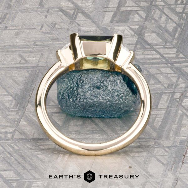 The "Dinara" ring in 14K yellow gold with 1.72-carat Australian sapphire The "Dinara" ring in 14K yellow gold, featuring a 1.72-carat Australian sapphire, stands upright on a textured stone background with the Earth’s Treasury logo at the bottom.