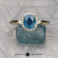 The "Eleanor" ring in 14K yellow gold features a 1.53-carat Montana sapphire, surrounded by small diamonds and displayed on rough blue crystal, with the “Earth’s Treasury” logo below.