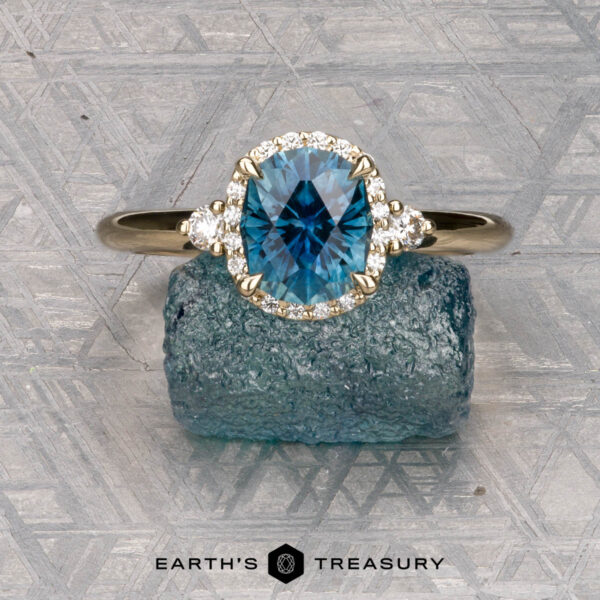 The "Eleanor" ring in 14K yellow gold with 1.53-carat Montana sapphire The "Eleanor" ring in 14K yellow gold features a 1.53-carat Montana sapphire, surrounded by small diamonds and displayed on rough blue crystal, with the “Earth’s Treasury” logo below.