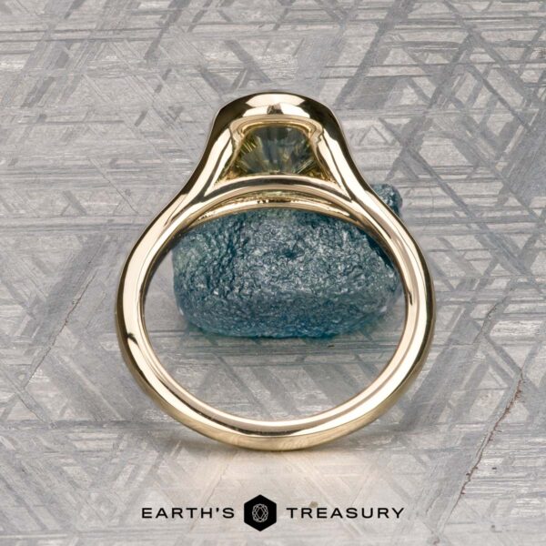 The "Brynn" ring in 14K yellow gold with 1.96-carat sapphire The "Brynn" ring in 14K yellow gold with a 1.96-carat sapphire stands upright on a textured metallic surface, with the "EARTH'S TREASURY" logo displayed at the bottom.