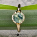 The "Brynn" ring in 14K yellow gold, featuring a 1.96-carat round light green sapphire, is displayed upright on a green leaf with the text "EARTH'S TREASURY" at the bottom.
