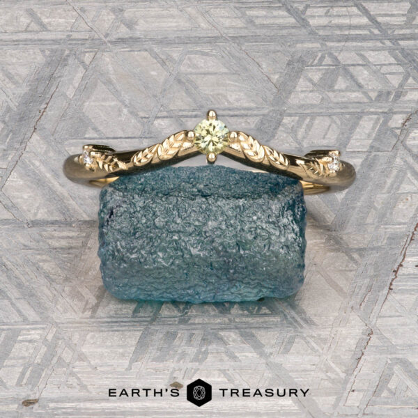 The "Aster" band in 14K yellow gold The "Aster" band in 14K yellow gold, featuring a yellow gemstone and leaf details, stands upright on a rough blue stone with the "Earth's Treasury" logo beneath.