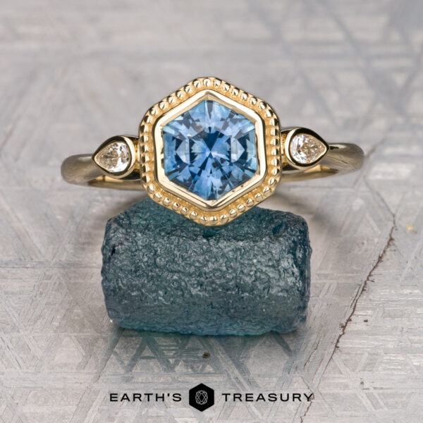 The "Sadie" ring in 14K yellow gold with 1.49-carat Montana sapphire The "Sadie" ring features a 1.49-carat Montana sapphire in a hexagon cut, accented by two small round diamonds and set in 14K yellow gold, displayed on a rough blue stone.