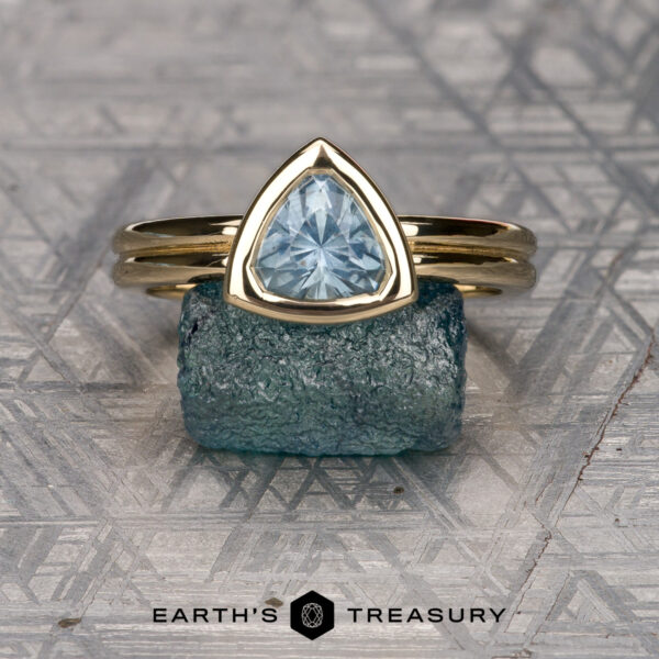 The "Lola" ring in 14k yellow gold with 1.22-carat Montana sapphire The "Lola" ring in 14k yellow gold with a 1.22-carat Montana sapphire is displayed on a rough blue stone, with the "Earth's Treasury" logo and text below.