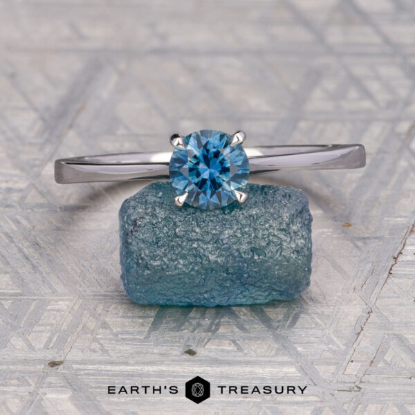The "Elena" ring in 14K white gold with 0.93-carat Montana sapphire The "Elena" ring in 14K white gold with a 0.93-carat Montana sapphire rests on a raw blue stone, with the "EARTH'S TREASURY" logo visible at the bottom.