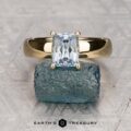 The "Davina" ring in 18K yellow gold with a 2.01-carat Montana sapphire is displayed atop a rough blue-green mineral, with the "Earth's Treasury" logo at the bottom.