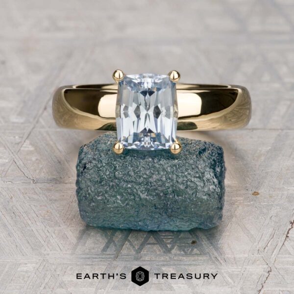 The "Davina" ring in 18K yellow gold with 2.01-carat Montana sapphire The "Davina" ring in 18K yellow gold with a 2.01-carat Montana sapphire is displayed atop a rough blue-green mineral, with the "Earth's Treasury" logo at the bottom.