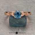 The "Kirryn" ring in 14K rose gold, featuring a 1.17-carat Montana sapphire and leaf motifs, is displayed upright on a rough blue stone background. Earth’s Treasury logo appears at the bottom.