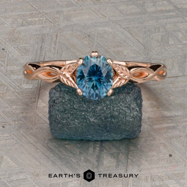 The "Kirryn" ring in 14K rose gold with 1.17-carat Montana sapphire The "Kirryn" ring in 14K rose gold, featuring a 1.17-carat Montana sapphire and leaf motifs, is displayed upright on a rough blue stone background. Earth’s Treasury logo appears at the bottom.