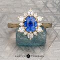 The "Angelica" ring in 14K yellow gold showcases a 1.54-carat Ceylon sapphire center, surrounded by sparkling diamonds and elegantly set against a textured blue stone background.