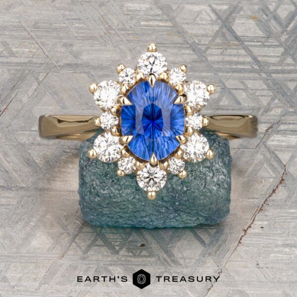 The "Angelica" ring in 14K yellow gold with 1.54-carat Ceylon sapphire The "Angelica" ring in 14K yellow gold showcases a 1.54-carat Ceylon sapphire center, surrounded by sparkling diamonds and elegantly set against a textured blue stone background.