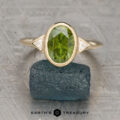 The "Ceres" ring in 18K yellow gold with a 2.93-carat Australian sapphire is displayed upright on a rough dark green mineral, with the Earth's Treasury logo beneath.