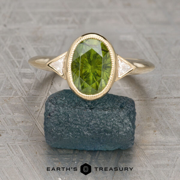 The "Ceres" ring in 18K yellow gold with 2.93-carat Australian sapphire The "Ceres" ring in 18K yellow gold with a 2.93-carat Australian sapphire is displayed upright on a rough dark green mineral, with the Earth's Treasury logo beneath.
