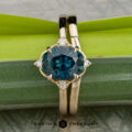 The "Marisol" ring in 14K yellow gold with a 2.36-carat Montana sapphire and the Custom-Fit Contour Band, both shown against green and gray textured backgrounds. Earth's Treasury logo appears at the bottom.