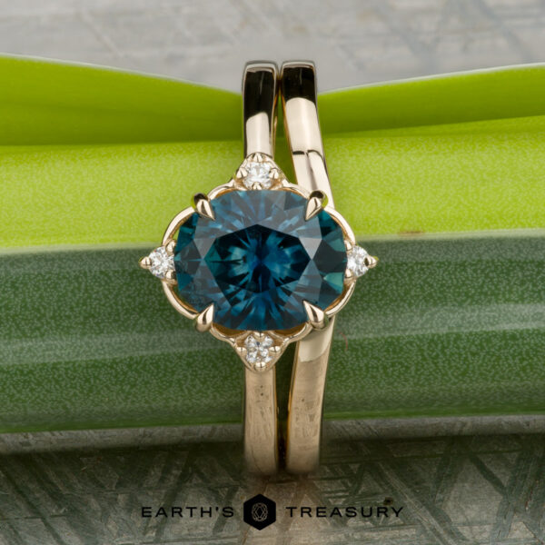 The "Marisol" ring in 14K yellow gold with 2.36-carat Montana sapphire, alongside the Custom-Fit Contour Band in 14K yellow gold The "Marisol" ring in 14K yellow gold with a 2.36-carat Montana sapphire and the Custom-Fit Contour Band, both shown against green and gray textured backgrounds. Earth's Treasury logo appears at the bottom.