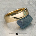 The "Logan" ring in 18K yellow gold, featuring an oval green gemstone, is displayed on a rough blue-green stone with the "EARTH'S TREASURY" logo beneath.