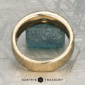 The "Logan" ring in 18K yellow gold, featuring an oval green gemstone, is displayed on a rough blue-green stone with the "EARTH'S TREASURY" logo beneath.
