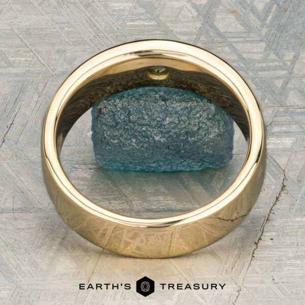 The "Logan" ring in 18K yellow gold The "Logan" ring in 18K yellow gold, featuring an oval green gemstone, is displayed on a rough blue-green stone with the "EARTH'S TREASURY" logo beneath.