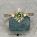 A ring with a round green gemstone and four small diamonds stands upright on a rough blue stone, with "Earth's Treasury" text below.