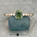 The "Blythe" ring in 14K yellow gold showcases a 0.90-carat Australian sapphire and diamond accents, displayed on a blue-green stone with the "Earth's Treasury" logo below.